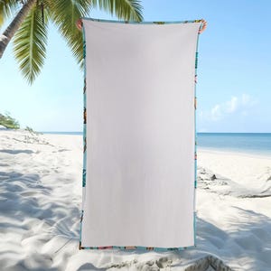 May include: A large white beach towel with a light blue border featuring a colorful tropical pattern. The towel is held up against a beach backdrop with palm trees, sand, and ocean.
