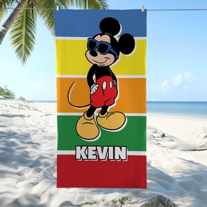 May include: A beach towel with a cartoon image of Mickey Mouse wearing sunglasses. The towel has horizontal stripes in blue, yellow, orange, green, and red. The name "KEVIN" is printed in white block letters at the bottom.