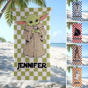 Puede incluir: Una toalla de playa rectangular con un patrón de cuadros verdes y blancos y una gran ilustración de una criatura verde con una túnica color canela. El nombre JENNIFER está impreso en letras negras en negrita en la parte inferior.