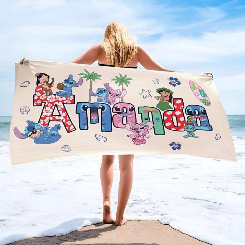 K&ouml;nnte beinhalten: Ein beiges Strandtuch mit dem Namen "Amanda" in bunten, stilisierten Buchstaben. Das Tuch ist mit Zeichentrickfiguren und tropischen Elementen wie Palmen, Blumen und einem Surfbrett verziert. Das Design ist vor dem Hintergrund von Meer und Himmel platziert.