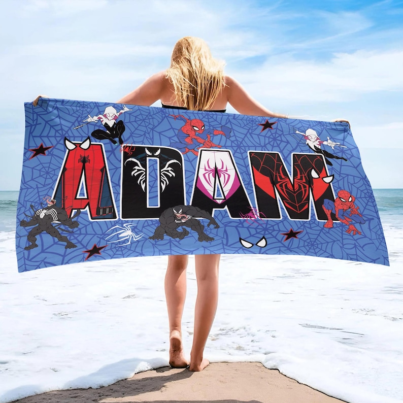 May include: Blue beach towel featuring the name "ADAM" in large, colorful letters with Spider-Man characters and web designs. The towel has a blue background with red stars and spider web patterns.