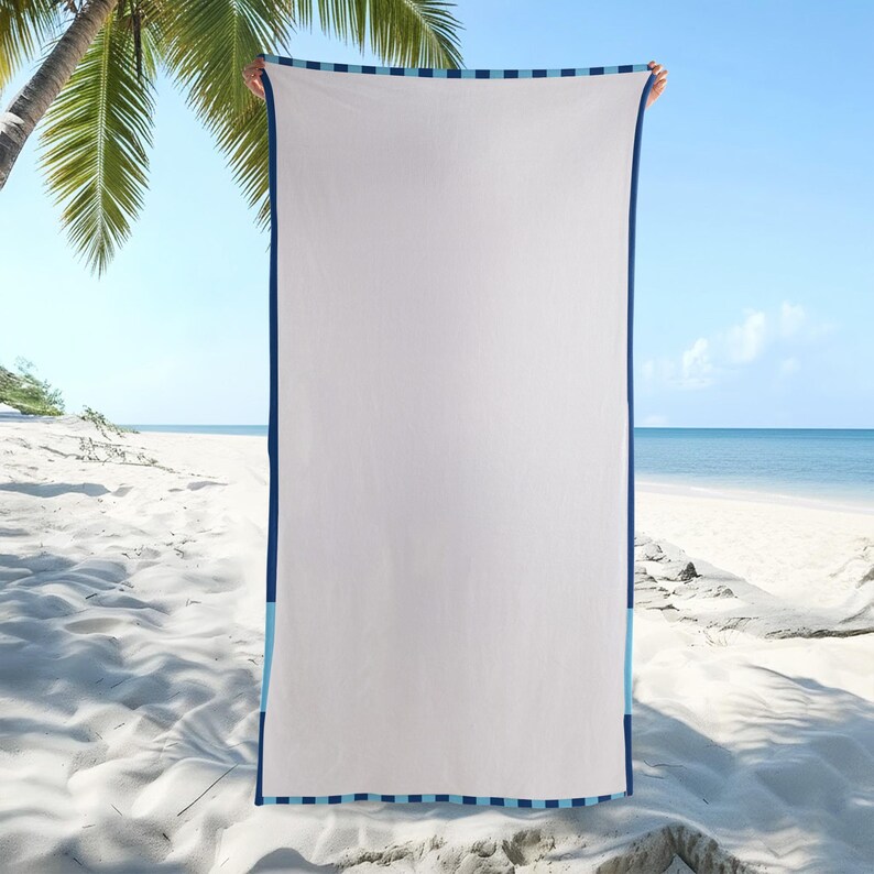 May include: A white beach towel with a navy blue border and light blue stripes. The towel is rectangular and held up against a beach backdrop with palm trees and ocean views.