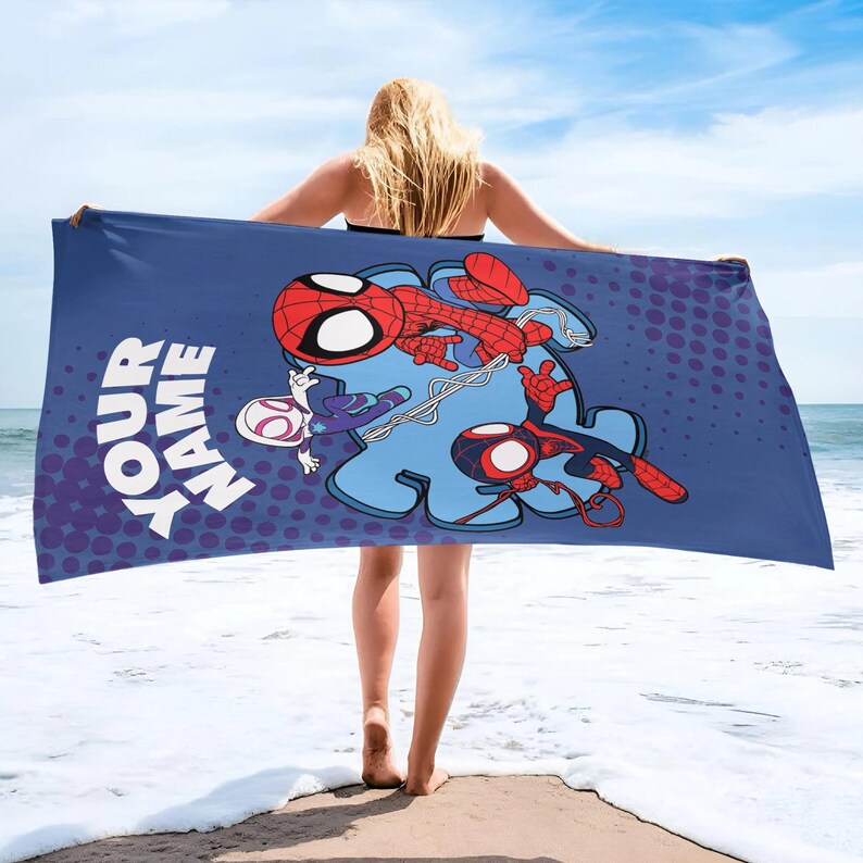May include: A blue beach towel featuring Spider-Man characters. The towel has a large graphic of Spider-Man in red and black, with the text "YOUR NAME" in white. The background includes a blue puzzle piece shape and a dotted purple pattern.