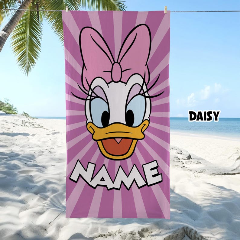 Puede incluir: Una toalla de playa rectangular con un gr&aacute;fico grande de Daisy Duck con un lazo rosa sobre un fondo de rayos de sol morados y rosas claros. La palabra NAME est&aacute; impresa en letras blancas grandes en la parte inferior y la palabra DAISY a la derecha.