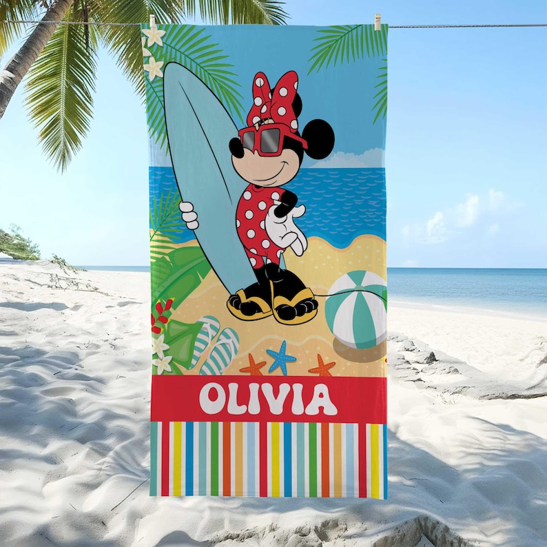 Puede incluir: Toalla de playa con Minnie Mouse con un traje de ba&ntilde;o de lunares rojos, gafas de sol y lazo, sosteniendo una tabla de surf. La toalla tiene un fondo de escena de playa con el nombre "OLIVIA" en letras blancas sobre una franja roja y rayas coloridas en la parte inferior.