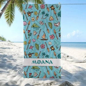 May include: A light blue beach towel with a repeating pattern of cartoon characters, flowers, and boats. The word "MOANA" is printed in white on a white band across the bottom. The towel is hanging on a clothesline with a beach and ocean in the background.