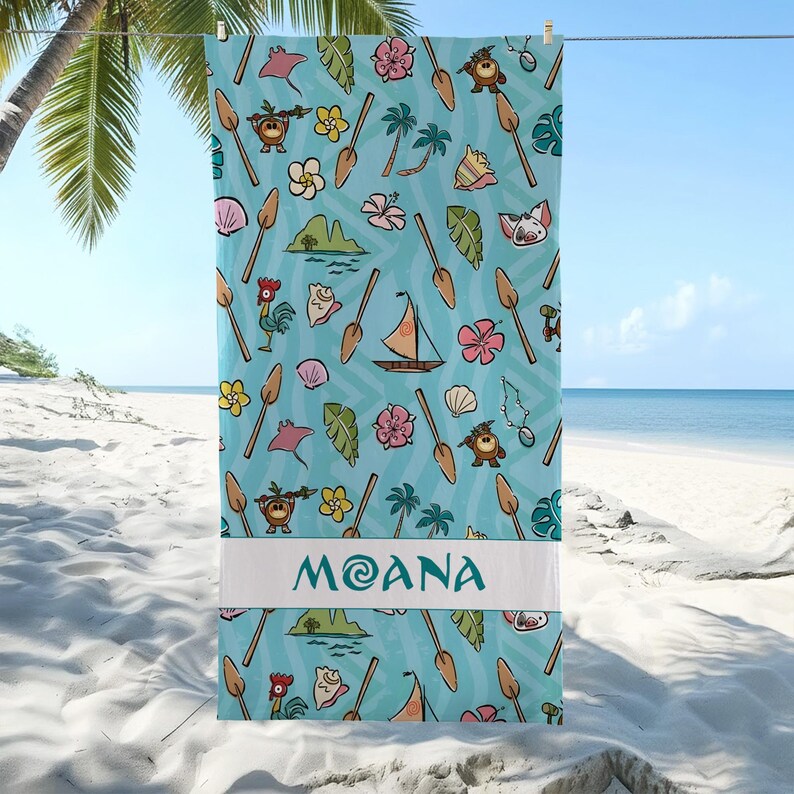 May include: A light blue beach towel with a repeating pattern of cartoon characters, flowers, and boats. The word "MOANA" is printed in white on a white band across the bottom. The towel is hanging on a clothesline with a beach and ocean in the background.
