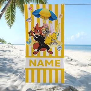 May include: Yellow and white striped beach towel featuring cartoon characters, a beach umbrella, and surfboards. The towel has the word "NAME" printed in large yellow letters on a white rectangular panel.