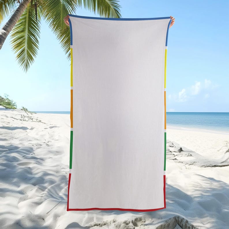 May include: A white beach towel with a blue border and vertical stripes in yellow, orange, green, and red. The towel is held up against a beach backdrop with palm trees and the ocean.