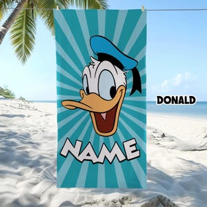 Puede incluir: Una toalla de playa rectangular con un gr&aacute;fico del rostro del Pato Donald centrado sobre un fondo de rayos de sol en color azul cerceta y blanco. La palabra NAME est&aacute; impresa en letras blancas grandes en la parte inferior y DONALD a la derecha.