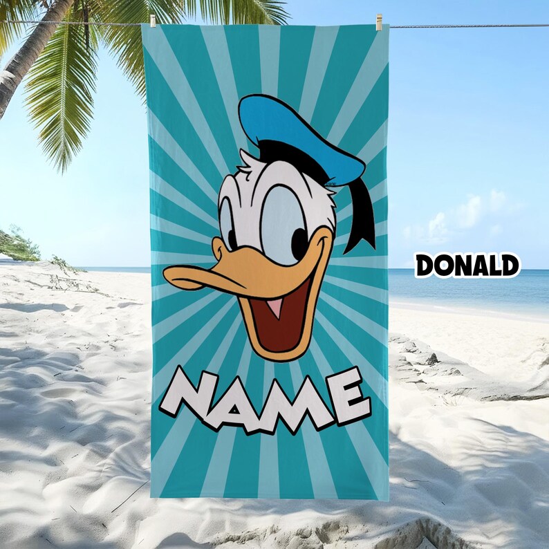 Puede incluir: Una toalla de playa rectangular con un gr&aacute;fico del rostro del Pato Donald centrado sobre un fondo de rayos de sol en color azul cerceta y blanco. La palabra NAME est&aacute; impresa en letras blancas grandes en la parte inferior y DONALD a la derecha.