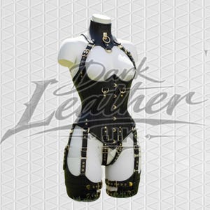 May include: Black leather corset with halter neck, multiple straps, and gold-colored hardware. The corset features a structured design with a high neckline and is displayed on a mannequin. The overall aesthetic is bold and edgy.