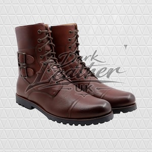Peut inclure: Une paire de bottes en cuir marron avec une finition texturée, un laçage avant avec des œillets métalliques et deux boucles latérales. Les bottes présentent un bout rapporté et une épaisse semelle crantée noire. Le texte Dark Leather UK est visible.