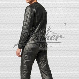 May include: A black leather jumpsuit featuring a quilted grid pattern throughout the entire garment. The long-sleeved one-piece suit has a round neckline and a fitted silhouette. The text Dark Leather UK is overlaid across the centre of the image.