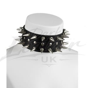 May include: A black leather choker necklace with silver-colored spikes. The choker is studded with multiple conical spikes around the entire circumference. The necklace is displayed on a white mannequin head, showcasing its punk rock or gothic style.