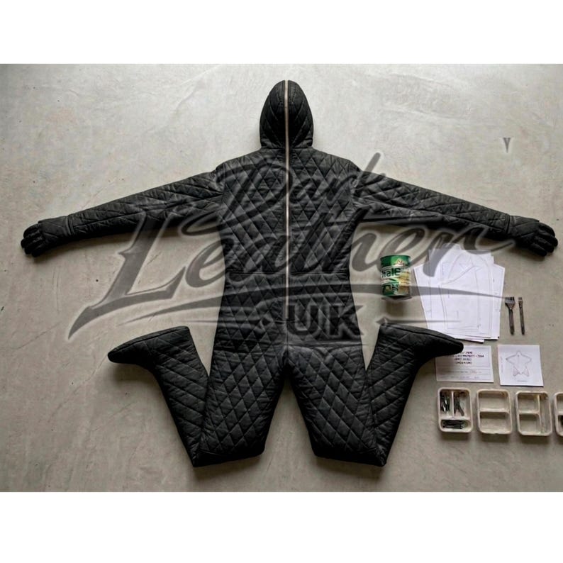 May include: A black quilted jumpsuit with a hood and a full-length zipper. The jumpsuit is laid out with arms and legs extended. The image also includes a can, papers, and small containers.