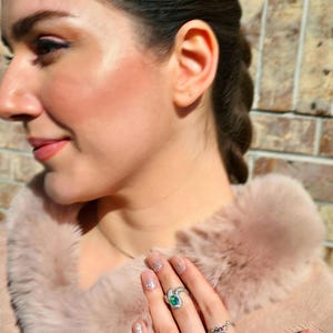 May include: Two silver rings worn on fingers. The upper ring features a single oval-shaped iridescent opal stone with a dark blue-green play of colour. The lower ring is a wider band set with multiple small, multicoloured opal stones.