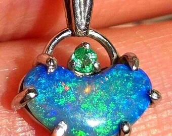 May include: A heart-shaped pendant featuring a blue opal, with green flashes, set in silver-toned metal. A small green gemstone sits above the opal. The pendant is a unique piece of jewellery.