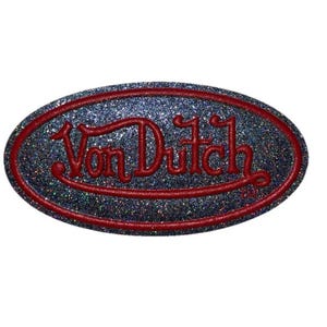 May include: An oval-shaped patch with the text "Von Dutch" in red script. The background is a glittery, dark blue color, and the border is a thin red line. The patch is likely for clothing or accessories.