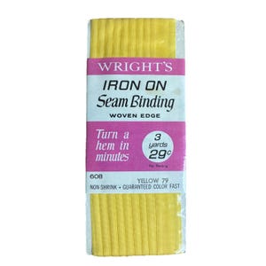 Könnte beinhalten: Eine Rolle gelbes Wright's Bügelband. Die Verpackung ist weiß und rosa mit dem Text "WRIGHT'S IRON ON Seam Binding" und "Turn a hem in minutes". Das Produkt ist 2,74 Meter lang.
