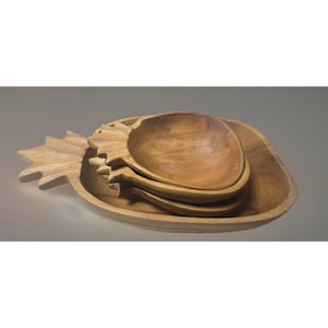 Pode incluir: Um conjunto de tigelas de madeira em forma de abacaxi. O conjunto inclui uma bandeja grande e várias tigelas menores que se encaixam. A madeira tem uma cor castanha clara natural e as tigelas estão vazias.