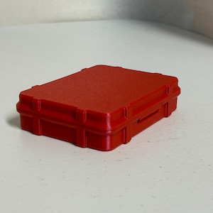 Peut inclure: Une petite boîte rectangulaire en plastique rouge avec une surface texturée. La boîte a un couvercle à charnière et un mécanisme de verrouillage sécurisé. La conception suggère un conteneur de protection pour petits objets ou équipements.