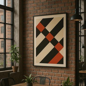 May include: A framed abstract art print with a geometric design in black, cream, and red. The artwork hangs on a brick wall in a room with a wooden table, metal chairs, and potted plants. The room has a window and pendant lights.