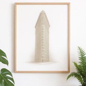 Puede incluir: Una impresión enmarcada del edificio Flatiron en la ciudad de Nueva York. La obra de arte es un boceto detallado en tonos beige y marrón, sobre un fondo blanco. El marco es de madera clara.