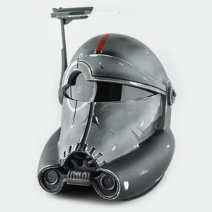 May include: A gray and black helmet with a red stripe and a visor. The helmet has a detailed design with a communication device attached. The helmet is likely a prop or collectible item.