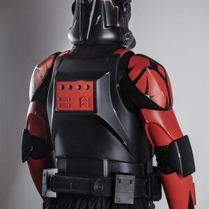 May include: A black and red costume, featuring a helmet with a crown-like design. The armour has red accents on the shoulders and arms, with a black belt and a black skirt. The costume is designed with a futuristic aesthetic.