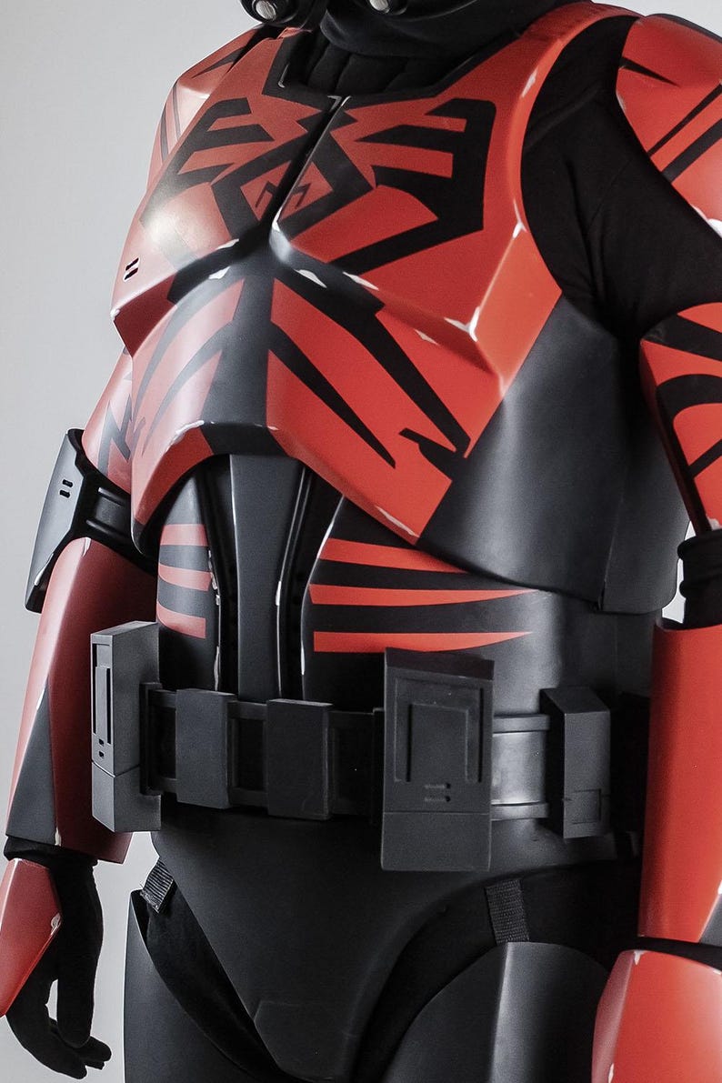 May include: A red and black armoured costume with detailed patterns. The chest and shoulder armour have bold, angular designs. The costume includes a utility belt and black under-layer, creating a striking contrast. The design suggests a futuristic or sci-fi theme.