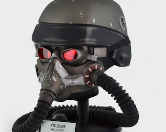 May include: A detailed, grey and black Killzone Helghast helmet with red-tinted lenses and a black visor. The helmet features a complex respirator and is displayed on a black stand. A small label reads "KILLZONE HELGHAST HELMET".