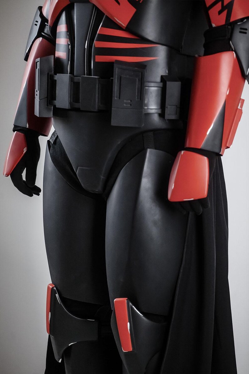 May include: A black and red armoured costume with a sleek design. The costume features red accents on the arms, shoulders, and knees, with a black belt and chest piece. The overall aesthetic suggests a futuristic or science fiction theme.