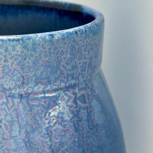 May include: A ceramic vessel featuring a crystalline glaze with a vibrant blue color palette. The surface displays intricate, star-like patterns created by the crystallization process, with subtle iridescent highlights and a smooth, glossy finish.