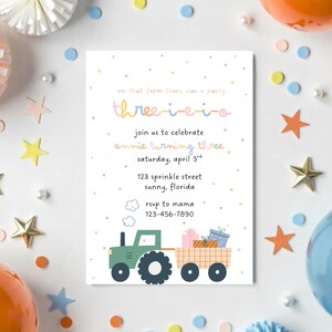 May include: A birthday party invitation with the text "three-i-e-i-o" in pastel colors. The invitation features a green tractor pulling a wagon with gifts. The invitation is surrounded by balloons, stars, and confetti.