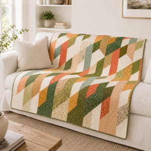 May include: A rectangular quilt featuring a geometric pattern of diagonal stripes in shades of orange, olive green, sage, and cream. The fabric displays various floral and textured prints, with visible machine quilting lines throughout the surface.