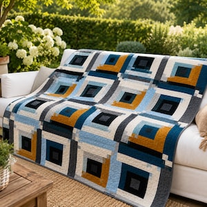 May include: A quilt featuring a repeating geometric pattern of nested squares in shades of navy blue, light blue, white, charcoal gray, and mustard yellow. The fabric has a visible quilted texture with stitched lines throughout the entire surface.