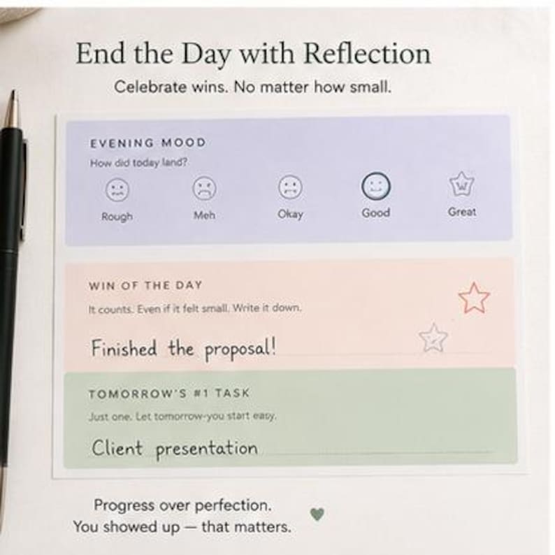 May include: A rectangular daily reflection notepad with a black pen. The page features sections titled End the Day with Reflection, Evening Mood with five emoji icons, Win of the Day with handwritten text Finished the proposal!, and Tomorrow's #1 Task.