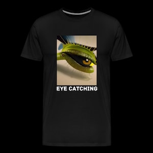 May include: A black t-shirt featuring a rectangular graphic of a green Venus flytrap with a human-like eye inside its jaws. The plant has spiky edges and a yellow iris. Below the graphic, the text EYE CATCHING is printed in white capital letters.