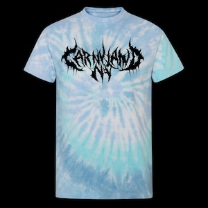 May include: A short-sleeve crew neck t-shirt featuring a light blue and white tie-dye pattern. The centre of the chest displays a black graphic with stylised, jagged lettering that reads CARNIVAND NY in a sharp, dark metal-inspired font style.