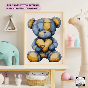May include: A framed cross stitch pattern featuring a blue and yellow patchwork teddy bear holding a yellow heart. The text at the top reads PDF CROSS STITCH PATTERN INSTANT DIGITAL DOWNLOAD. The design is displayed in a light wood frame.