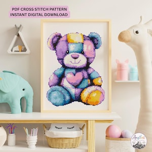 May include: A framed cross stitch pattern featuring a pixelated teddy bear with a patchwork design in shades of purple, blue, pink, and yellow. The bear has a heart on its chest and a patch on its head. Text at the top reads PDF CROSS STITCH PATTERN INSTANT DIGITAL DOWNLOAD.