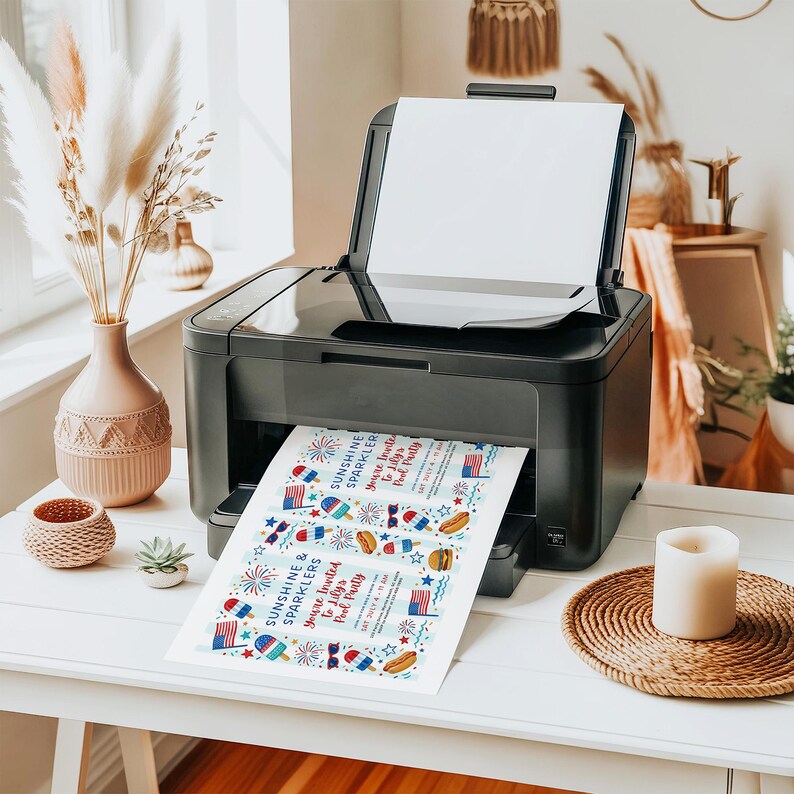 Peut inclure: Une imprimante noire imprime des invitations sur le th&egrave;me patriotique. Les invitations pr&eacute;sentent des graphiques rouges, blancs et bleus de feux d'artifice, de drapeaux et de glaces. Le texte sur les invitations se lit "Sunshine & Sparklers, You're Invited to Lily's Pool Party."