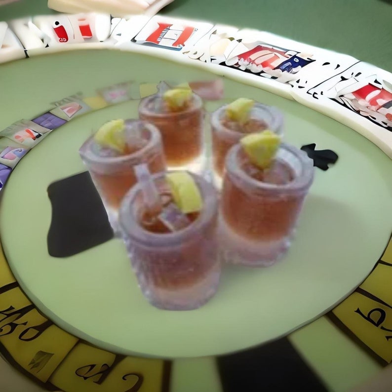 May include: Four clear glass shot glasses filled with a brown liquid and garnished with lemon wedges. The glasses are arranged in a circle on a green surface with a black and white game board in the background.