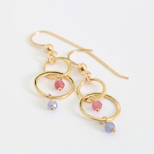 May include: Gold earrings with two interlocking circles and pink and purple gemstone beads.
