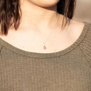 Puede incluir: Primer plano de una mujer con un su&eacute;ter verde, un collar de cadena plateada y un colgante de piedra rosa.