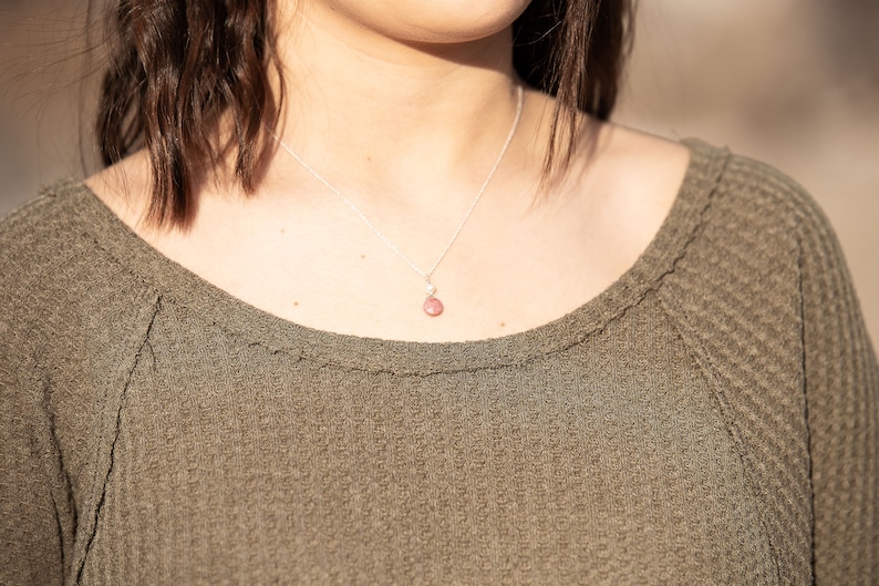 Puede incluir: Primer plano de una mujer con un su&eacute;ter verde, un collar de cadena plateada y un colgante de piedra rosa.
