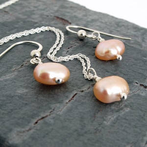 May include: A set of delicate pearl earrings and a matching necklace. The pearls are a soft pink color and are attached to silver chains.