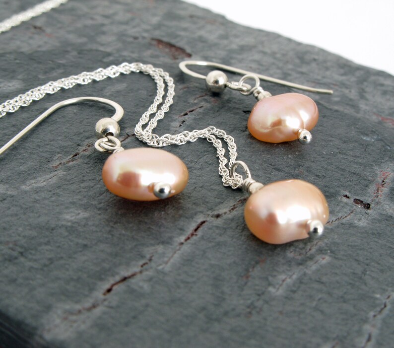 May include: A set of delicate pearl earrings and a matching necklace. The pearls are a soft pink color and are attached to silver chains.