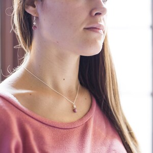 Puede incluir: Una mujer con un su&eacute;ter rosa con un collar de cadena plateada y un peque&ntilde;o colgante de piedra rosa. Tambi&eacute;n lleva pendientes plateados con una peque&ntilde;a piedra rosa.